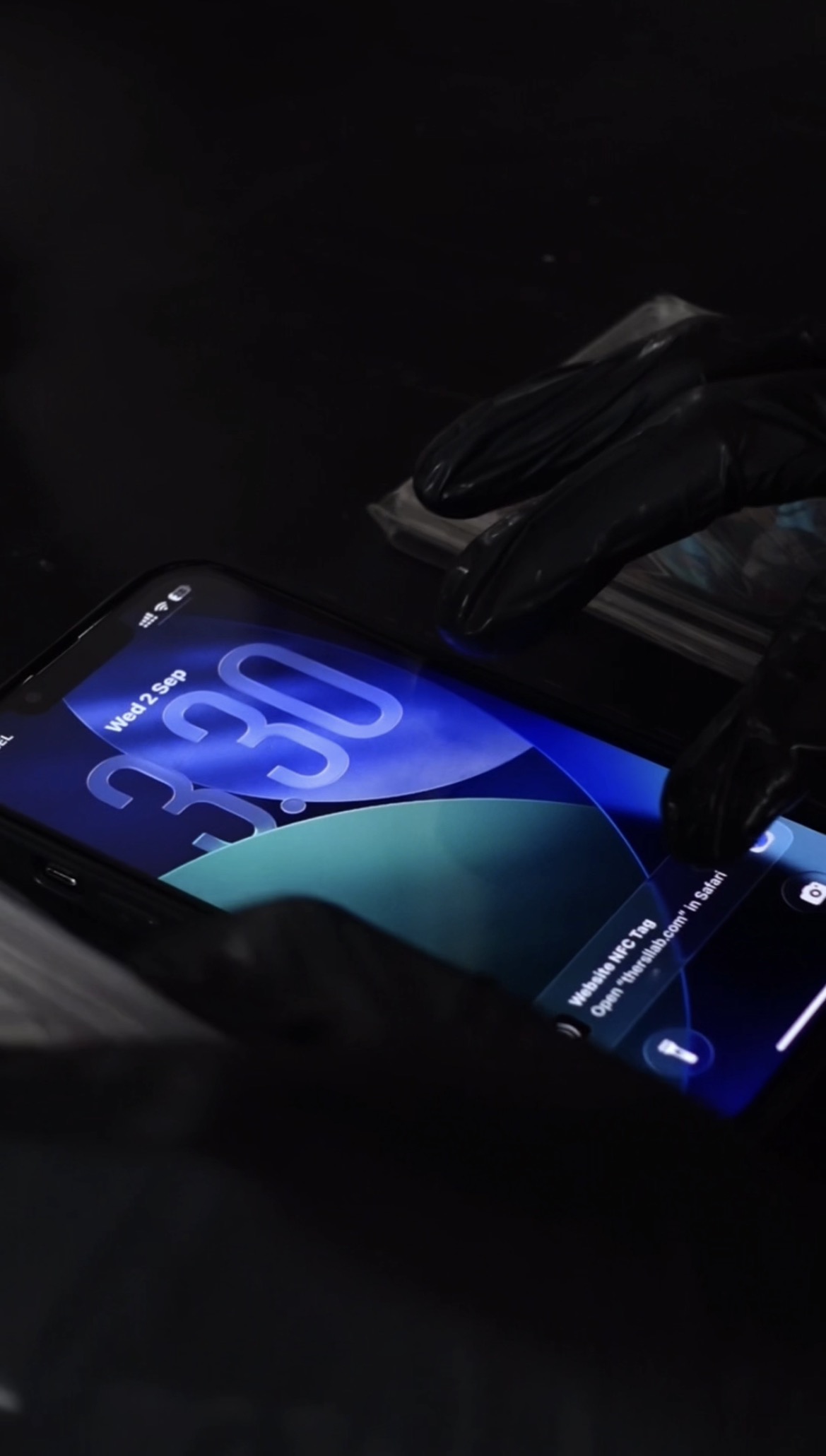 Gloved hand tapping a graded slab's NFC chip to a phone, opening thersllab.com